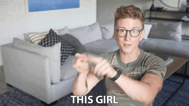 a man wearing glasses and a watch says " this girl " in front of a couch