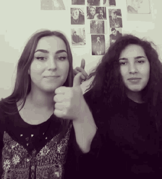 two girls giving a thumbs up in front of a wall with pictures