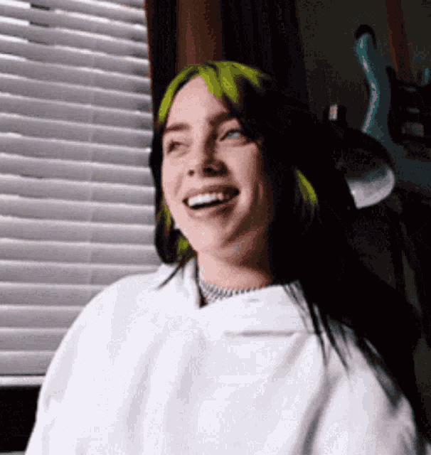 a woman with green hair is smiling while sitting in front of a window