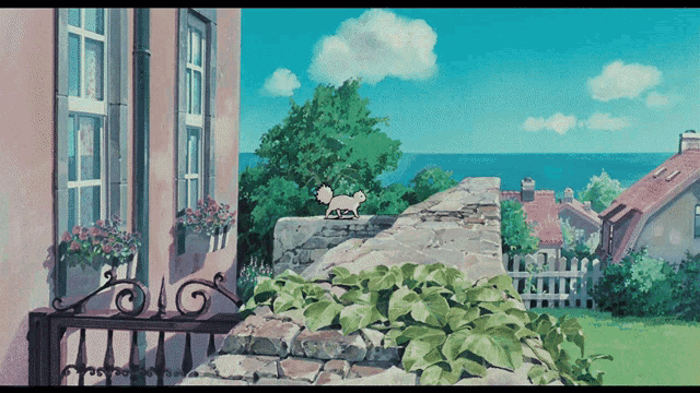 a cat sits on a stone wall in front of a house with a view of the ocean