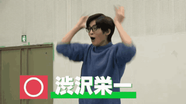 a man wearing glasses and a blue sweater stands in front of a green exit sign