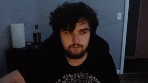 a man with a beard is wearing headphones and a black shirt while sitting in a chair .