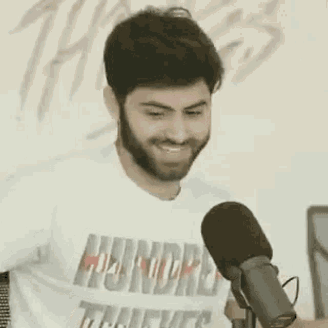 a man with a beard is smiling in front of a microphone while wearing a white shirt .
