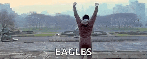 a man is standing on a ledge with his arms in the air and the word eagles written on the bottom .