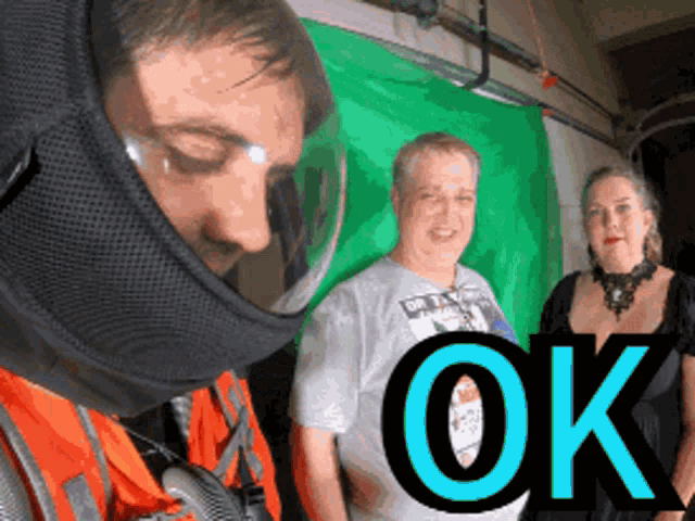 a man wearing a helmet stands in front of a green screen with the word ok in blue