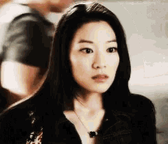 a woman with long black hair is wearing a black shirt and a black necklace