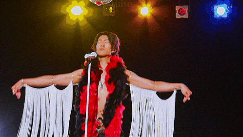 a man singing into a microphone while wearing a red boa