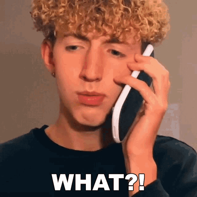 a young man with curly hair is talking on a cell phone and has the words what written on his face
