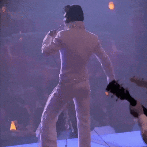a man in a white suit is singing into a microphone in front of a crowd .