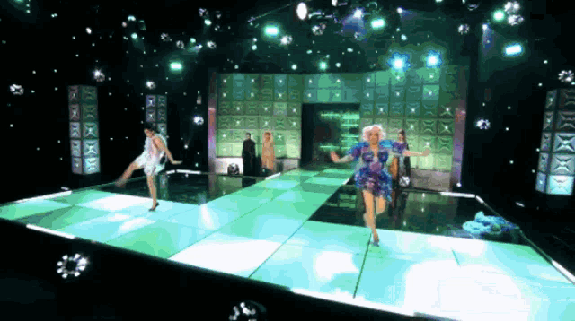 a group of women are dancing on a stage with a sign that says ' x ' on it