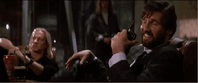 a man in a suit and tie is holding a gun and smiling