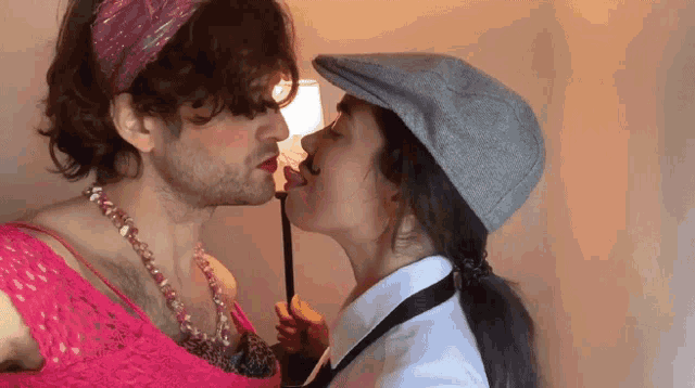 a man in a pink top and a woman in a gray hat kissing