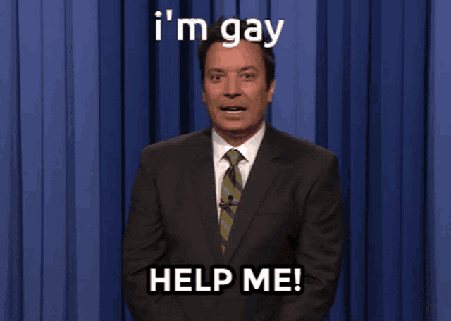 a man in a suit and tie stands in front of a blue curtain and says " i 'm gay help me "