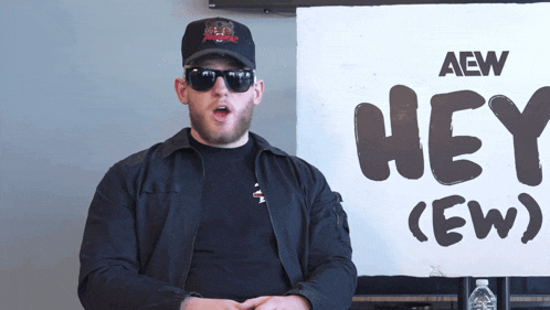 a man wearing sunglasses stands in front of a sign that says hey