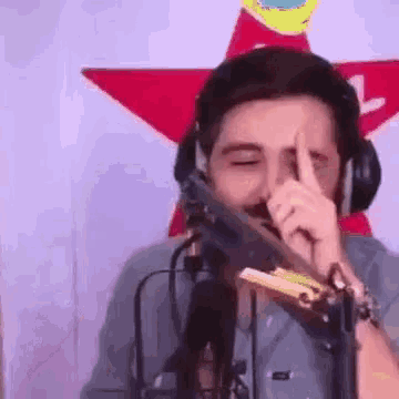 a man wearing headphones is holding a gun in front of a microphone and making a funny face .