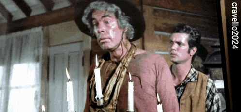 a man in a cowboy hat stands next to a man with candles on his chest