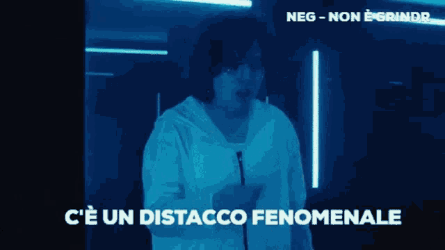 a man in a white hoodie is standing in a dark room with the words " c'e un distacco fenomenale " on the screen