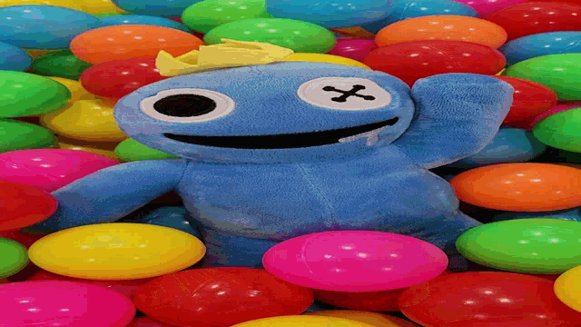 a stuffed animal with a cross on its face is laying in a pile of colorful balls