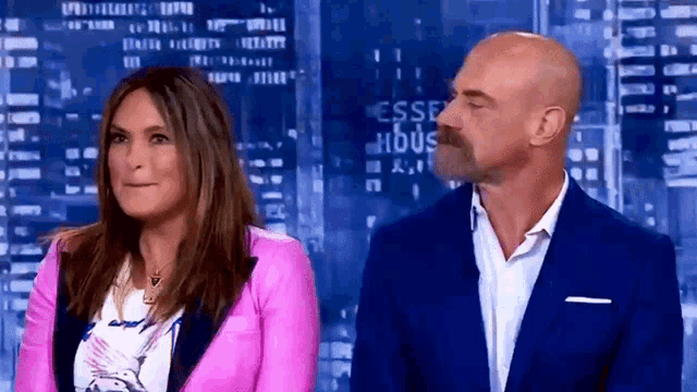 a man in a blue suit and a woman in a pink jacket are standing next to each other on a television show .