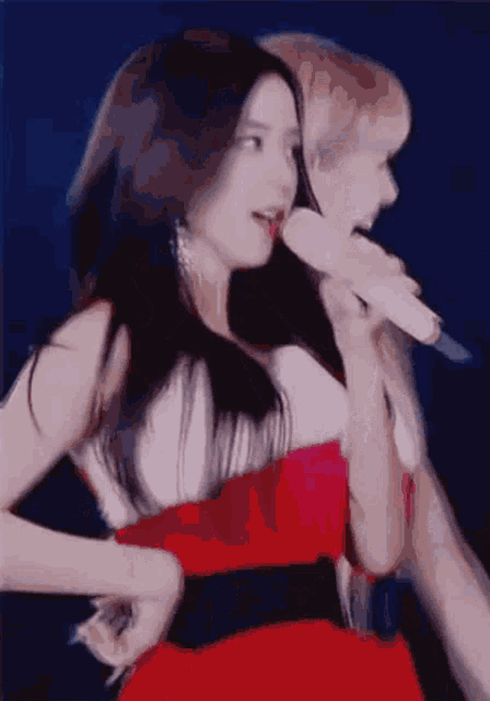 a woman in a red dress is singing into a microphone while another woman holds a microphone .