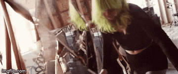 a woman with green hair is standing in front of a mirror and looking at herself .