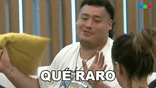 a man is holding a yellow pillow and says que raro in spanish .