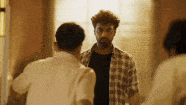 a man in a plaid shirt is talking to another man in a black shirt .