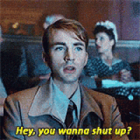 a man in a suit and tie is sitting in a classroom talking to someone .