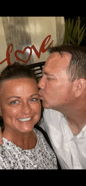 a man is kissing a woman on the cheek in front of a love sign