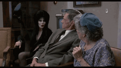 a woman in a black dress is sitting next to a man and woman