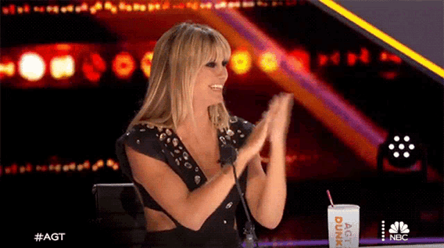 a woman applauds while sitting next to a dunkin donuts cup