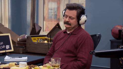 a man wearing headphones sits at a desk with a sign that says cheese club