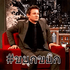 a man in a suit and tie is sitting in a red chair with a caption in a foreign language