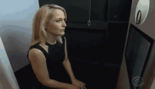 a woman in a black dress is sitting in a dark room looking at herself in a mirror .