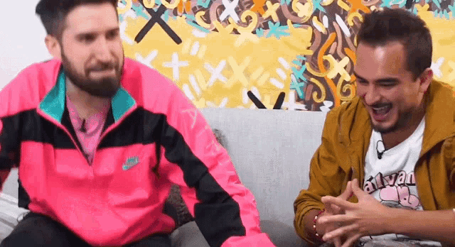 two men are sitting on a couch and one of them is wearing a pink nike jacket .