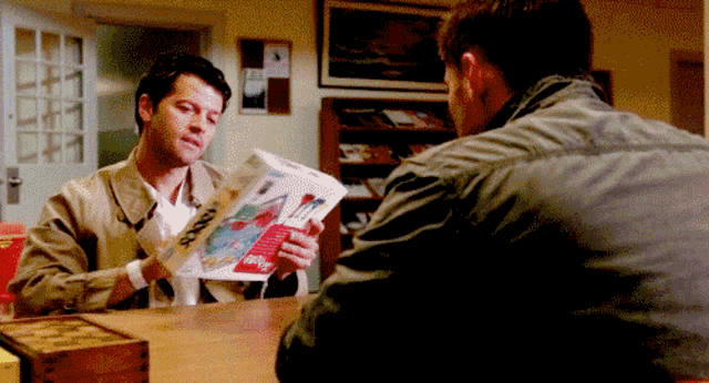 two men are sitting at a table and one of them is holding a piece of paper that says ' a ' on it