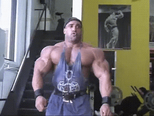 a muscular man in a blue tank top is standing in front of a yellow wall