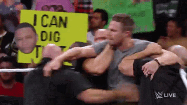 a man in a wrestling ring holds a sign that says i can dig