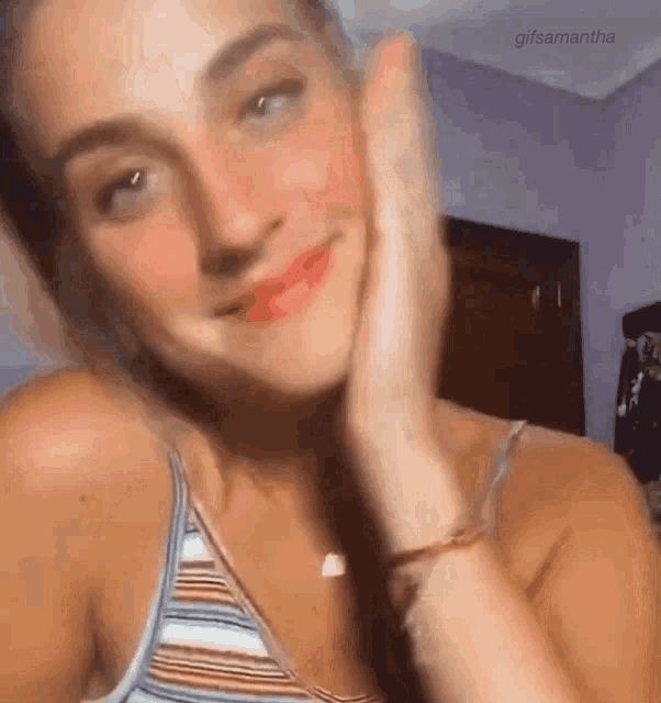 a woman in a striped tank top is smiling and touching her face .