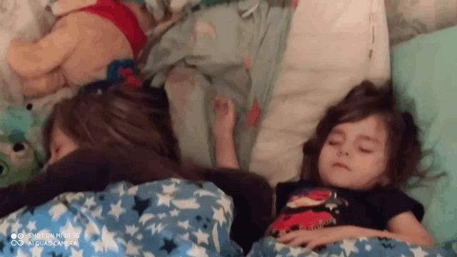two little girls are sleeping on a bed with a blanket that has stars on it .