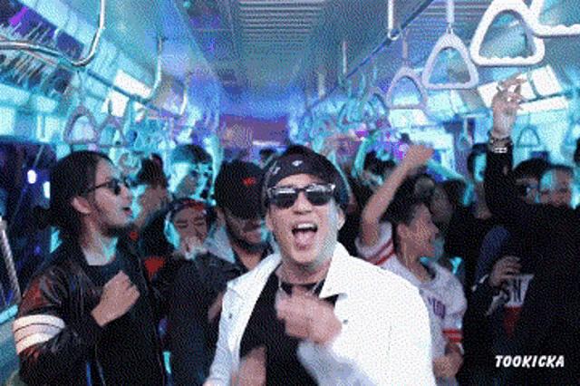 a man wearing sunglasses is dancing on a subway with a crowd of people behind him and the words tookicka below him