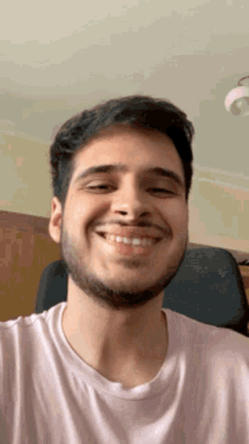 a man with a beard wearing a pink shirt smiles for the camera
