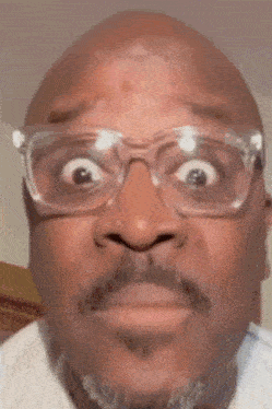 a close up of a bald man wearing glasses and making a funny face .