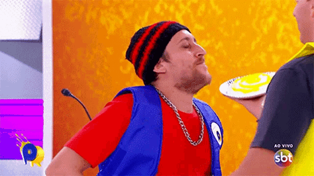 a man wearing a red shirt and a blue vest is holding a plate of food ..