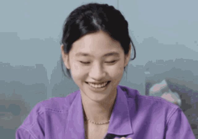 a woman in a purple shirt is smiling while looking at her phone