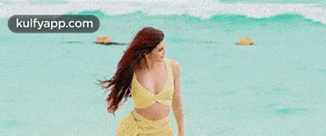 a woman in a yellow crop top and skirt is walking on a beach .