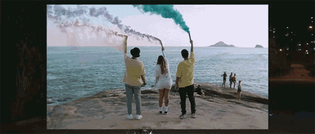 a group of people are standing on a beach holding smoke bombs