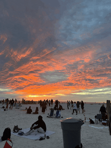 a large group of people are gathered on the beach at sunset