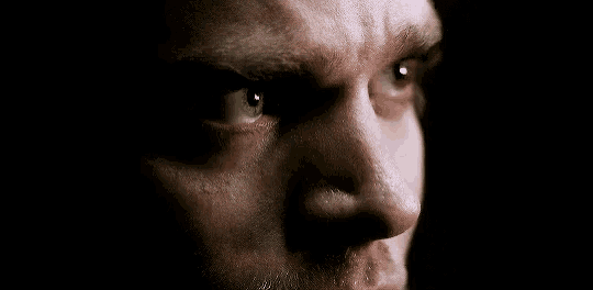 a close up of a man 's face with a beard and a serious look on his face .