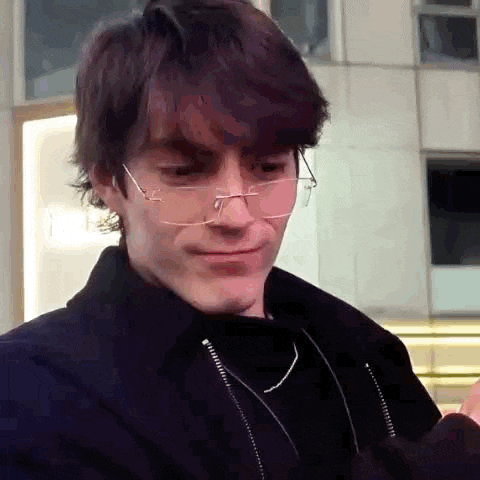 a young man wearing glasses and a black jacket is making a face .